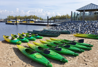 Varios kayaks verdes alineados en la arena, cerca de un embarcadero en Oesterdam Resort, Países Bajos.