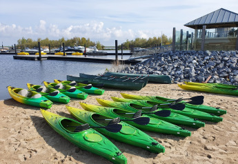 Mehrere grüne Kajaks am Sandstrand mit Bootsanleger im Hintergrund, aufgenommen bei Oesterdam Resort.