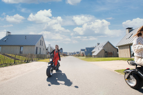 Mujer conduce un scooter por un barrio de casas pequeñas en Villa Oesterdam, en Oesterdam Resort, Países Bajos.