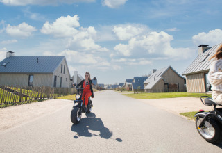 Woman rides a scooter through a modern tiny house neighborhood at Villa Oesterdam in Oesterdam Resort, Netherlands.