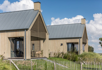 Two modern wooden tiny houses at Villa Oesterdam, Oesterdam Resort, Netherlands, on green lawns under blue sky.