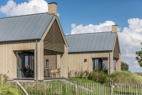 Zwei moderne Tiny Houses aus Holz im Oesterdam Resort, Niederlande, mit grüner Landschaft und blauem Himmel.