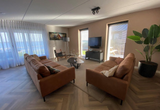 Wohnzimmer mit zwei braunen Sofas, großen Fenstern und Zimmerpflanze in der Villa Oesterdam Comfort Extra, Oesterdam Resort.