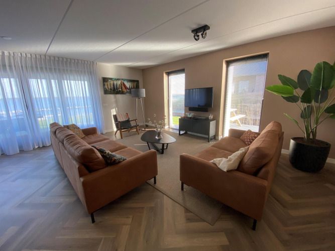 Salon avec deux canapés marron, grandes fenêtres et plante verte à la Villa Oesterdam Comfort Extra, Oesterdam Resort.