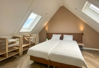 Habitación abuhardillada con dos camas, ventanas en el techo y estanterías de madera en Villa Oesterdam Comfort Extra, Oesterdam Resort, Países Bajos.