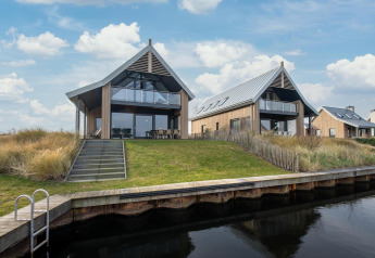 To moderne villaer ved vandet på Oesterdam Resort i Holland, omgivet af grønne bakker og blå himmel.
