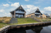Twee moderne waterwoningen op Oesterdam Resort in Nederland met grasheuvels en privéaanlegsteiger.