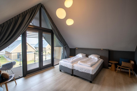 Dormitorio moderno con grandes ventanales y balcón en Villa Oesterdam Deluxe, Oesterdam Resort, Países Bajos.