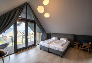 Dormitorio moderno con grandes ventanales y balcón en Villa Oesterdam Deluxe, Oesterdam Resort, Países Bajos.
