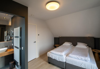 Schlafzimmer in der Villa Oesterdam Deluxe im Oesterdam Resort mit zwei Einzelbetten und modernem Bad.