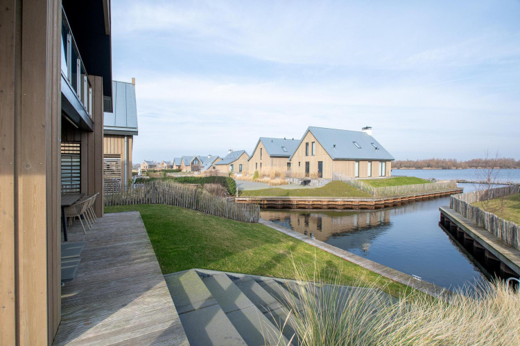 Vista de la Villa Oesterdam Deluxe en Oesterdam Resort, Países Bajos, con casas modernas junto al agua.