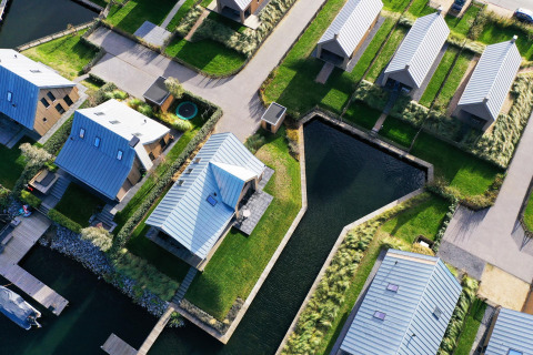 Luchtbeeld van moderne lodges met metalen daken en waterpartijen bij Villa Oesterdam, Oesterdam Resort, Nederland.