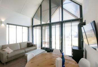 Salon moderne et lumineux à la Villa Oesterdam, Oesterdam Resort, Pays-Bas, avec de grandes fenêtres et un canapé.