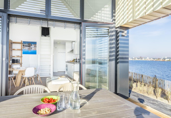 Lodge moderne Villa Oesterdam avec terrasse face à l'eau à l'Oesterdam Resort, Pays-Bas, journée ensoleillée.