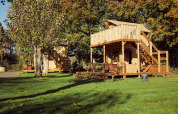 Tienda de glamping Arriba en Resort de Parel, Países Bajos, con terraza de madera y árboles verdes.