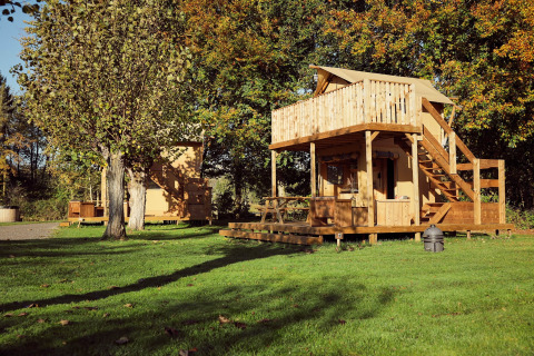 Tienda de glamping Arriba en Resort de Parel, Países Bajos, con terraza de madera y árboles verdes.