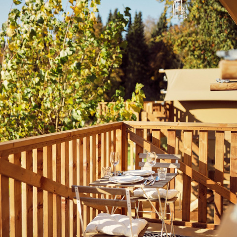 Gemütlicher Essplatz mit Holzmöbeln auf der Veranda eines Safarizelts im Resort de Parel, Niederlande.