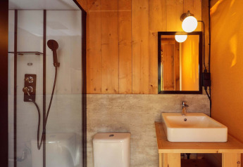 Bagno moderno nella tenda glamping Arriba con pareti in legno, doccia in vetro, WC e lavabo quadrato.