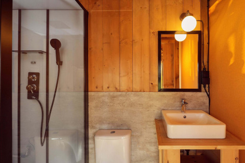 Baño moderno dentro de la tienda safari Arriba con paredes de madera, ducha de vidrio, inodoro y lavabo cuadrado.