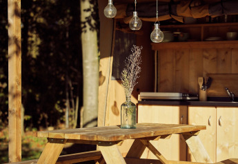 Tavolo da picnic in legno con vaso e fiori secchi sotto una tenda glamping al Resort de Parel nei Paesi Bassi.