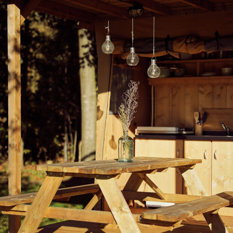 Wooden picnic table with a vase and dried flowers under a glamping tent at Resort de Parel, Netherlands.