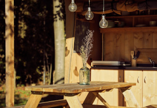 Table de pique-nique en bois avec un vase et des fleurs séchées sous une tente glamping au Resort de Parel.
