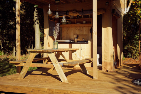 Holztisch mit Bank vor einem gemütlichen Safarizelt mit Küche im Resort de Parel, Niederlande.