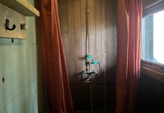 Ducha rústica con paneles de madera, cortinas naranjas y luces en el techo en un alojamiento glamping.
