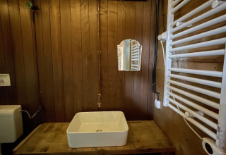Glamping badkamer met houten wanden, vierkante wasbak, klein muurtje spiegel en sfeerverlichting.