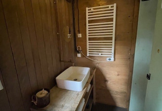 Baño acogedor con paredes de madera, lavabo, radiador toallero y luces de techo en un sitio de glamping.