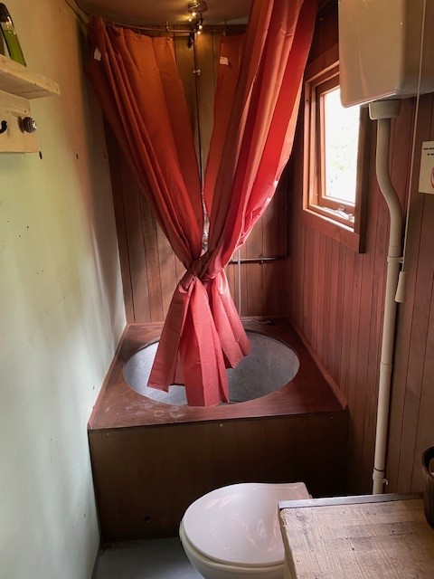 Baño de glamping con bañera redonda de madera, cortina de ducha roja y un inodoro en primer plano.
