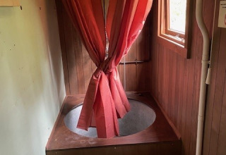 Glampingbadkamer met een ronde houten badkuip, een rood douchegordijn en een toilet op de voorgrond.
