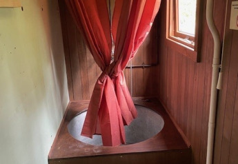Salle de bain glamping avec une baignoire ronde en bois, un rideau de douche rouge et des toilettes devant.