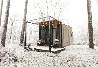 Sweet Cabin at Cosy Cabins, Limburg forest, Belgium, covered in snow with string lights on the porch.
