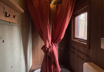 Acogedor cuarto de baño en la casa del árbol con bañera circular, cortinas de ducha rojas, luces de cuerda y paredes y ventana de madera.