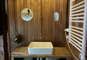 Rustic tree house bathroom with a wooden sink counter, square basin, round mirrors, and string lights above.