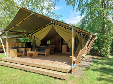Lodge de tienda safari con instalaciones sanitarias, terraza de madera y asientos cómodos en entorno verde.