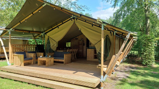 Lodge de tienda safari con instalaciones sanitarias, terraza de madera y asientos cómodos en entorno verde.