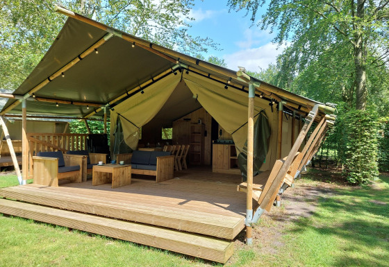 Lodge de tienda safari con instalaciones sanitarias, terraza de madera y asientos cómodos en entorno verde.