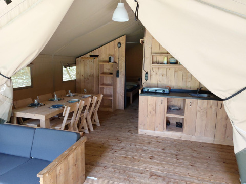 Vue intérieure d'une tente safari avec meubles en bois, salle à manger, coin cuisine et chambre aux Pays-Bas.