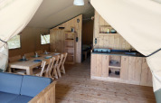 Vista interior de una tienda safari con muebles de madera, mesa de comedor, cocina y dormitorio en Países Bajos.