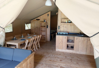 Binnenaanzicht van een safaritent met houten meubels, eettafel, keukenblok en slaapkamer in Nederland.