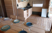 Vista interior de una tienda safari con mesa de comedor, cocina y nevera en Camping de Beukenhof.