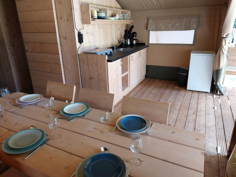 Interior view of a safari tent lodge with dining table, kitchen, and fridge at Camping de Beukenhof.