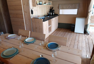 Vista interior de una tienda safari con mesa de comedor, cocina y nevera en Camping de Beukenhof.