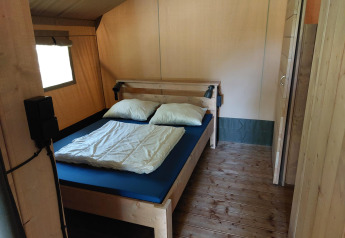 Interior de una tienda safari con instalaciones sanitarias en Camping de Beukenhof, Países Bajos, con cama.