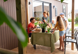 Familie isst gemeinsam auf einer Holzterrasse vor einer Lodge, sommerliche Atmosphäre im Garten.