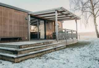 Cabaña de madera con terraza cubierta y nieve en Family Lodge, Holiday park De Boshoek, Países Bajos.