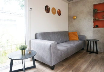 Stue i Family lodge på Holiday park De Boshoek i Holland med grå sofa, bord og orange pude.