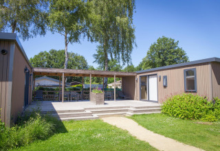 Family Lodge op Holiday park De Boshoek in Nederland, houten terras met stoelen en groene tuin.